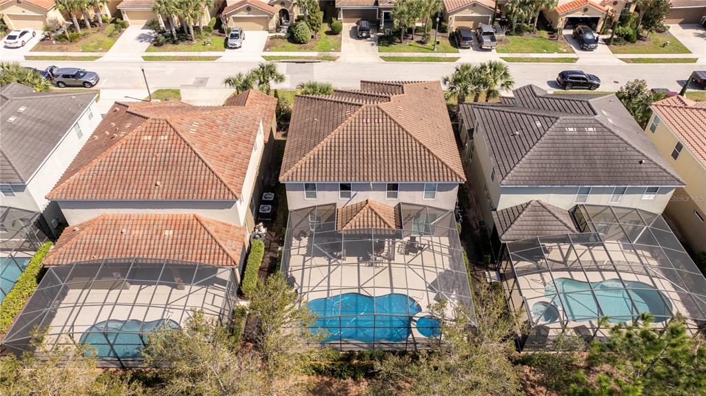 An aerial view shows three houses with screened-in pools and tile roofs in a suburban neighborhood — 5251 WILDWOOD WAY, DAVENPORT, FL