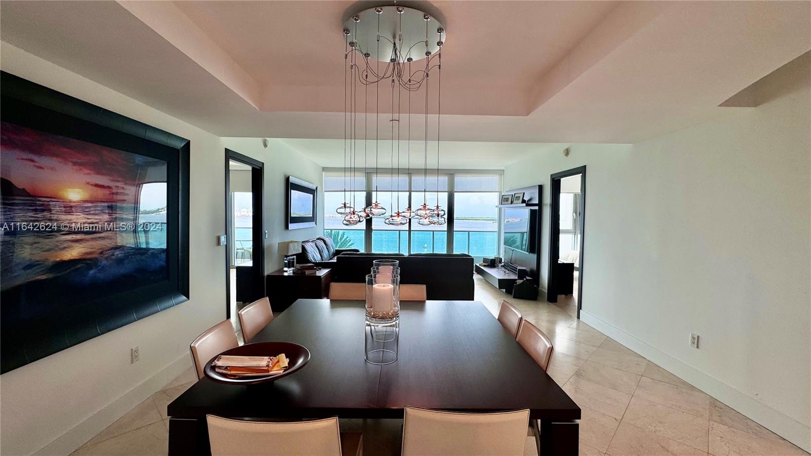 A dining area with a dark table and modern chandelier overlooks a living room and ocean — 1331 Brickell Bay Dr # 1109, Miami FL 33131, MIAMI, FL