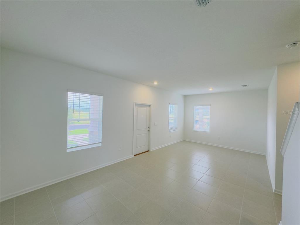 An empty room with white walls, tile flooring, and three windows near an entry door — 5872 MEDITATION DRIVE, CLERMONT, FL