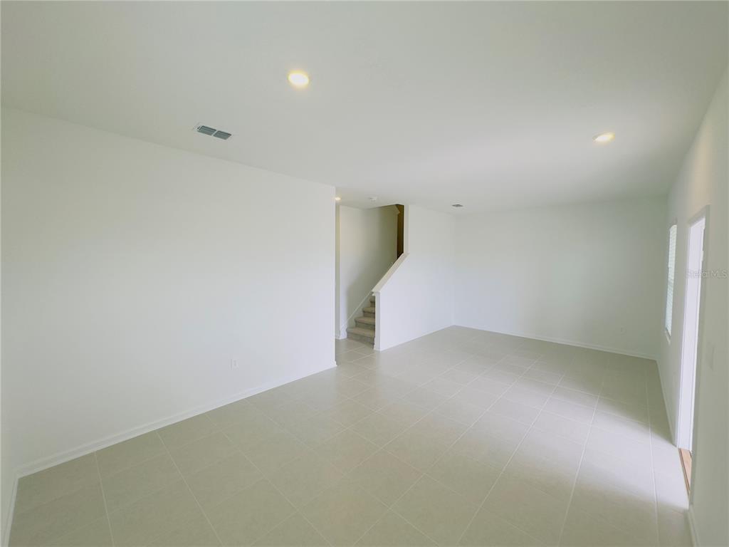 An empty room with white walls, tile flooring, recessed lighting, and a staircase in back — 5872 MEDITATION DRIVE, CLERMONT, FL
