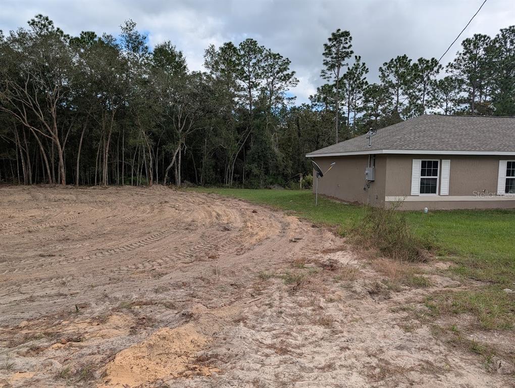 A side view of a house exterior next to a cleared, sandy lot with trees — Lot 9 SW 79TH TERRACE, OCALA, FL