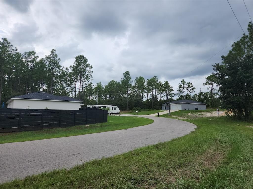 A paved road curves past a house with a black fence and a parked camper — Lot 9 SW 79TH TERRACE, OCALA, FL