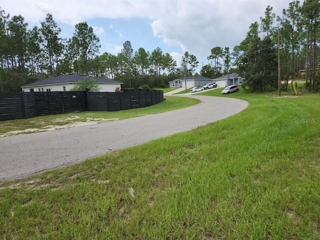 A curved asphalt road leads past a black wooden fence toward houses and pine trees — Lot 9 SW 79TH TERRACE, OCALA, FL