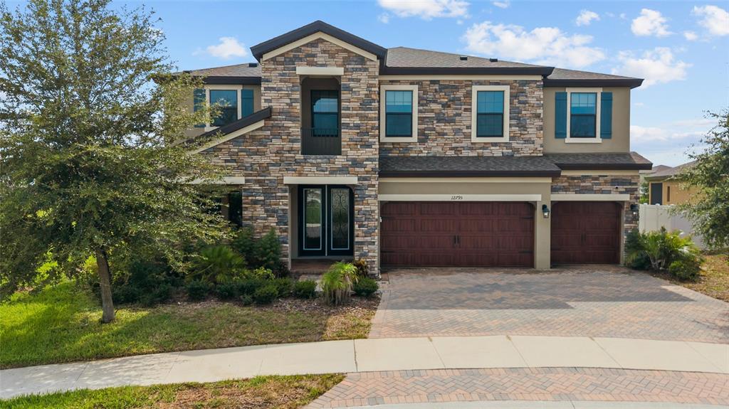 A two-story house with a stone facade, a three-car garage, and a paved driveway — 12795 FISHERVILLE WAY, RIVERVIEW, FL