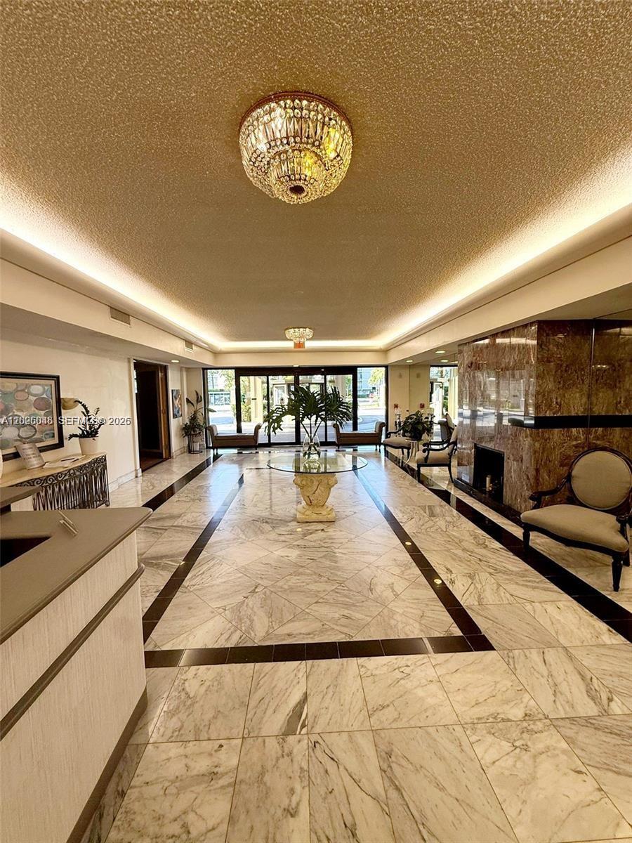 A marble-floored lobby features a crystal chandelier, a fireplace, and glass sliding doors — 800 NE 195th St # 720, Miami FL 33179, MIAMI, FL