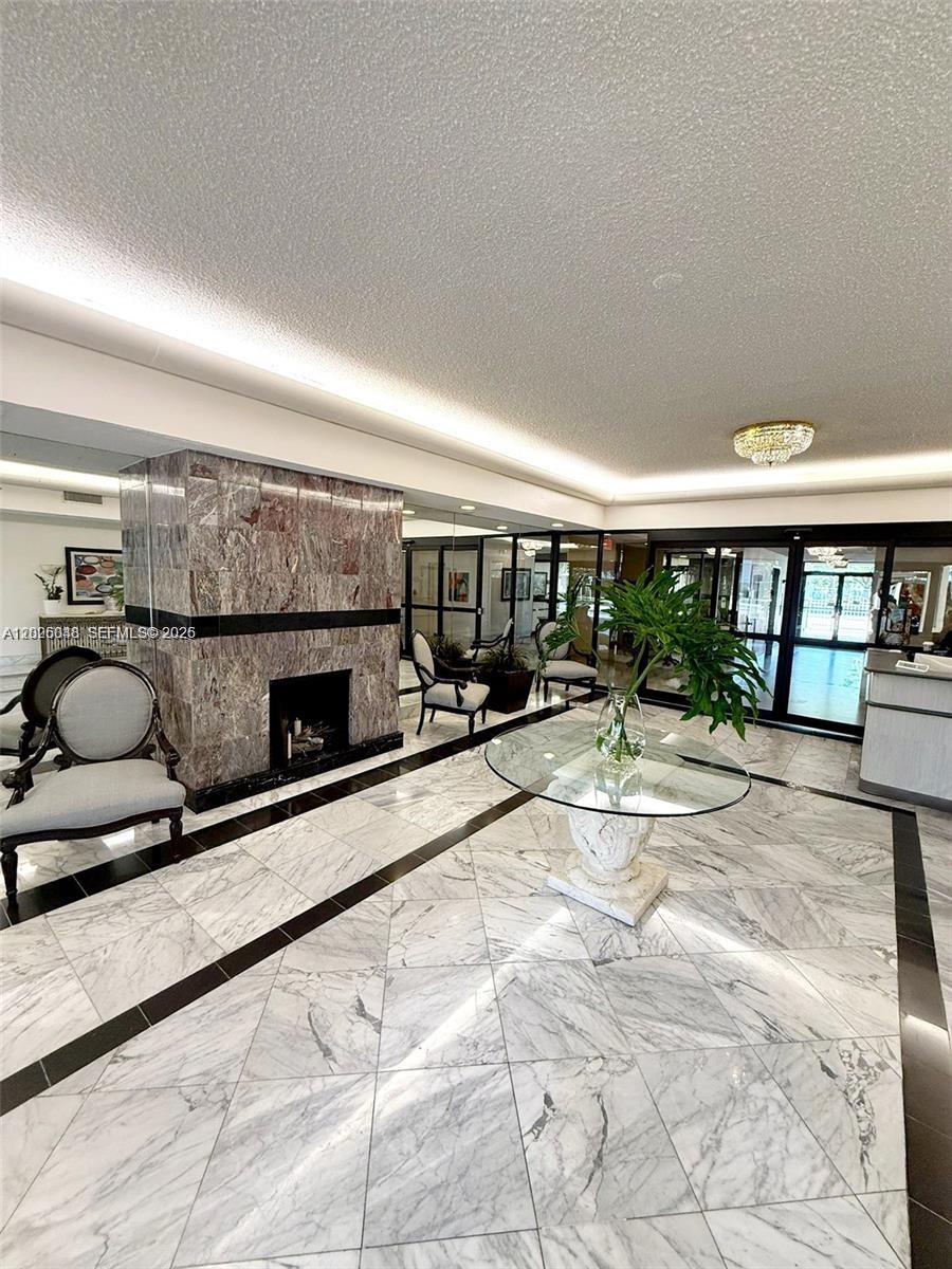 A lobby features a marble fireplace, tile flooring, and a glass-topped pedestal table — 800 NE 195th St # 720, Miami FL 33179, MIAMI, FL