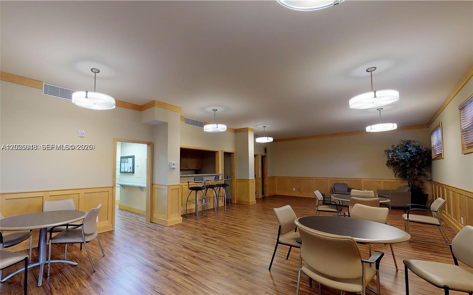 A spacious community room features wood-look flooring, beige walls with wainscoting, and multiple dining tables — 800 NE 195th St # 720, Miami FL 33179, MIAMI, FL
