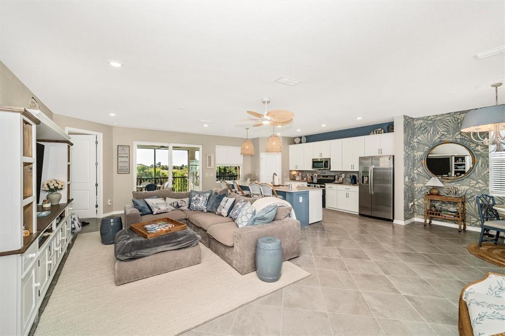 An open-concept living room and kitchen featuring tile floors, a sectional sofa, and white cabinetry — 17740 BORACAY COURT UNIT 202, VENICE, FL