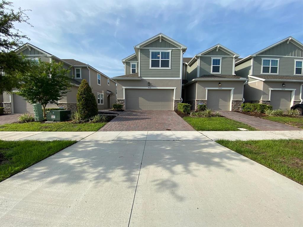 A row of two-story suburban townhomes features beige siding, stone accents, and paved driveways — 9076 OCEAN TIDE WAY, KISSIMMEE, FL