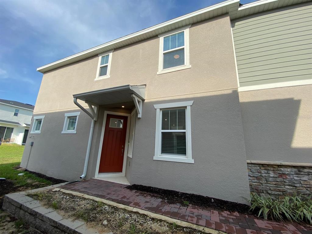 A two-story house exterior features a red front door, stucco siding, and stone accents — 9076 OCEAN TIDE WAY, KISSIMMEE, FL
