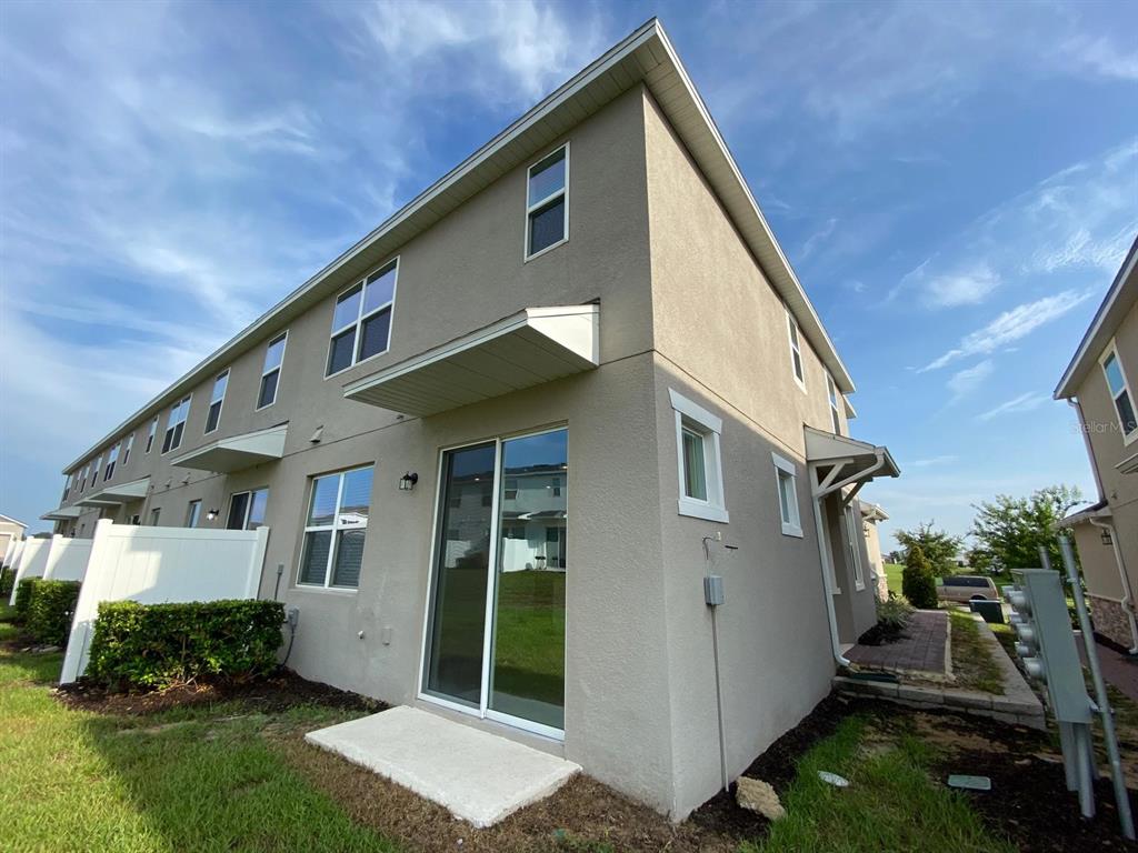 The exterior rear view of a two-story townhouse features a sliding glass door and patio — 9076 OCEAN TIDE WAY, KISSIMMEE, FL