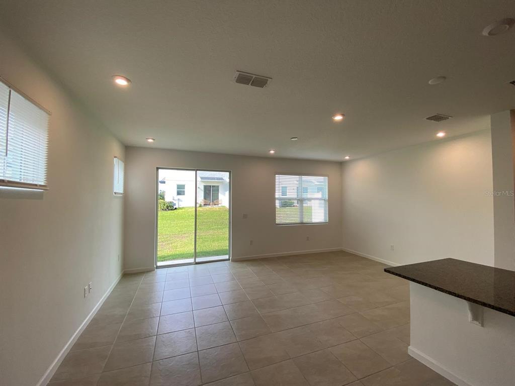 An empty living room features tile flooring, recessed lighting, a sliding glass door, and windows — 9076 OCEAN TIDE WAY, KISSIMMEE, FL