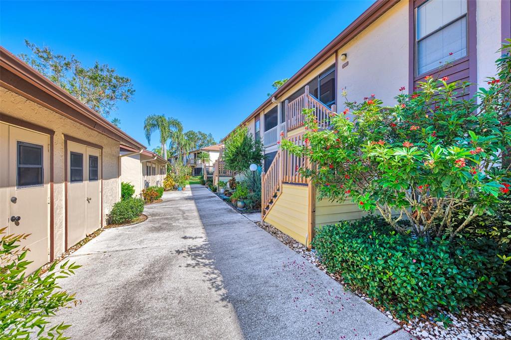 A concrete walkway leads between two apartment buildings with exterior stairs and lush landscaping — 5761 AVISTA DRIVE UNIT 5761, SARASOTA, FL