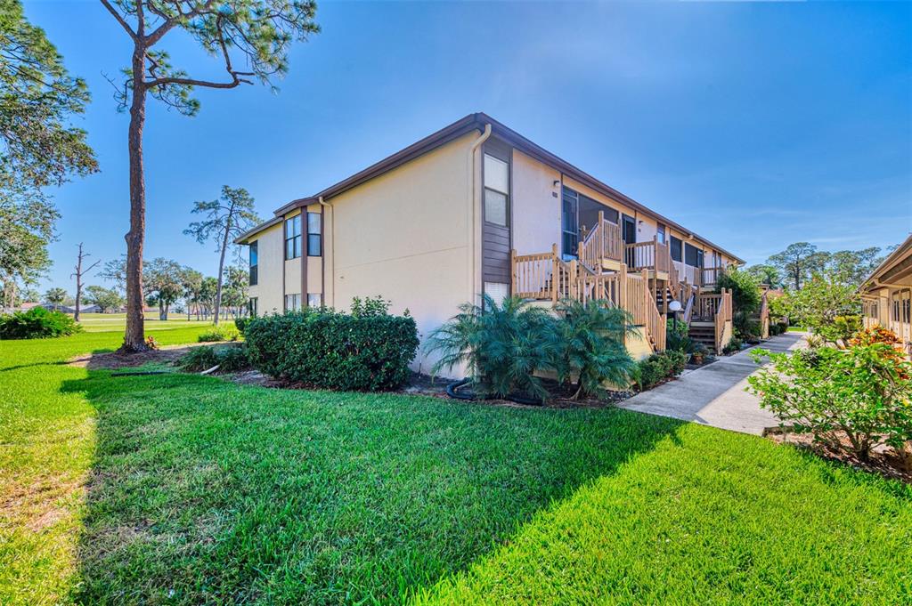 A two-story apartment building with wooden staircases and balconies sits beside a grassy lawn — 5761 AVISTA DRIVE UNIT 5761, SARASOTA, FL