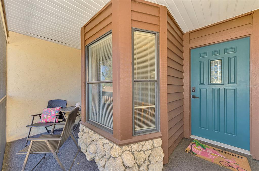 A covered porch features a teal front door, stone siding, and outdoor chairs — 5761 AVISTA DRIVE UNIT 5761, SARASOTA, FL