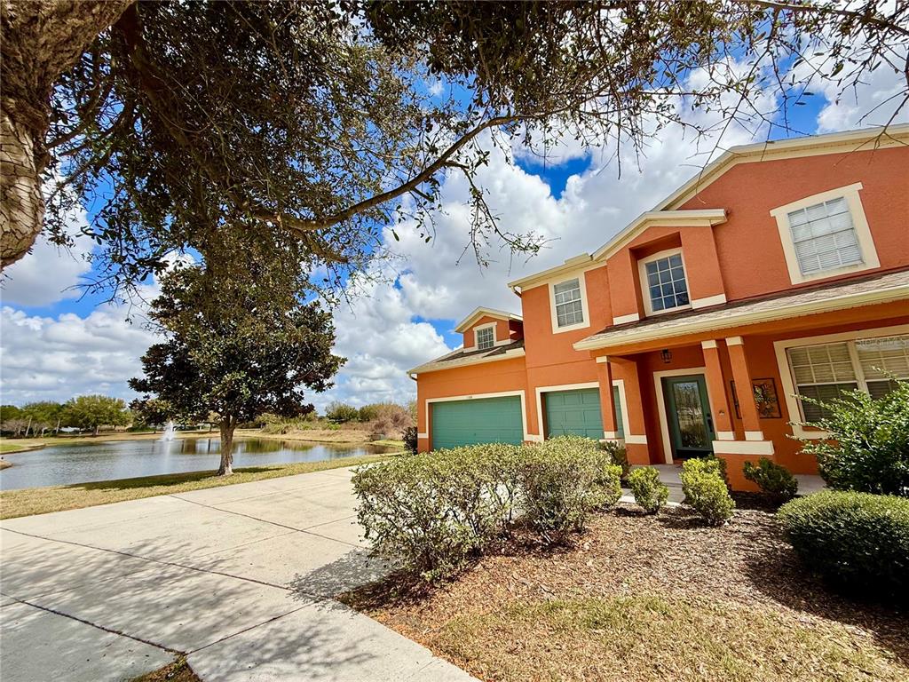 A two-story orange house with a two-car garage sits beside a pond — 11338 LAUREL BROOK COURT, RIVERVIEW, FL