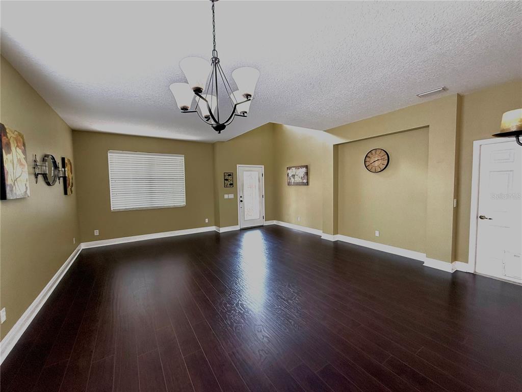 A spacious room with dark wood floors, tan walls, a chandelier, and a white door — 11338 LAUREL BROOK COURT, RIVERVIEW, FL