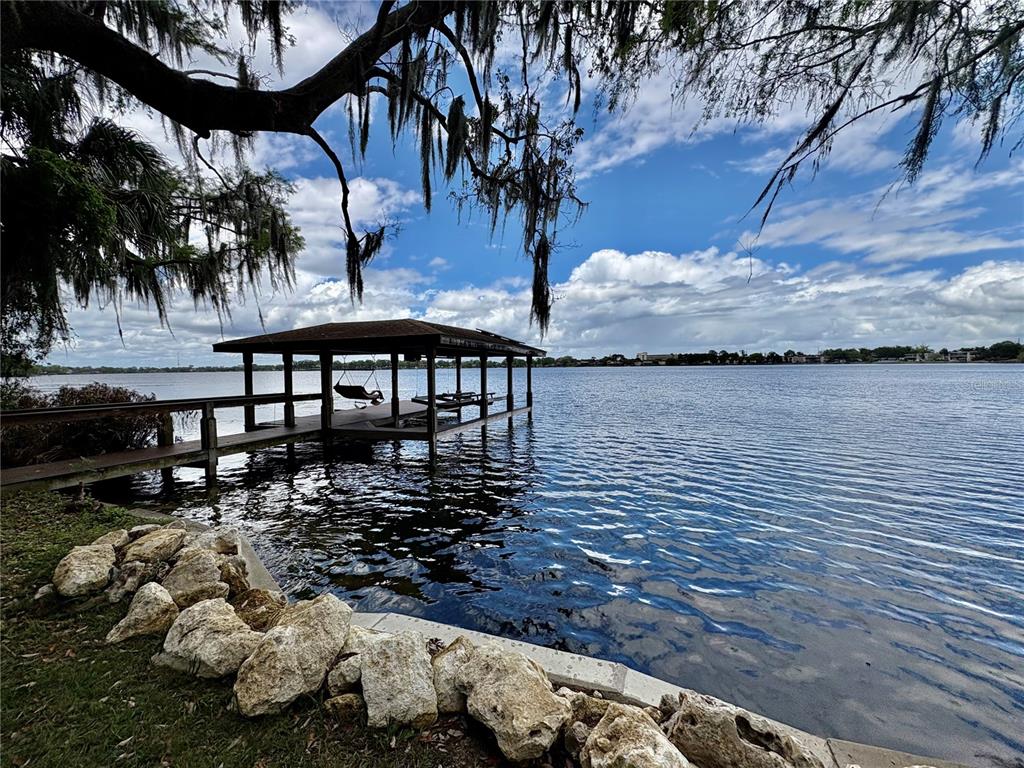 A wooden boat dock with a roof extends into a lake from a rocky shoreline — 438 LAKEVIEW AVENUE, WINTER PARK, FL