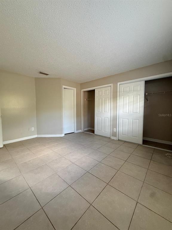 A bedroom with beige walls, light-colored tile flooring, and two sets of white closet doors — 965 BRYAN COURT, LONGWOOD, FL