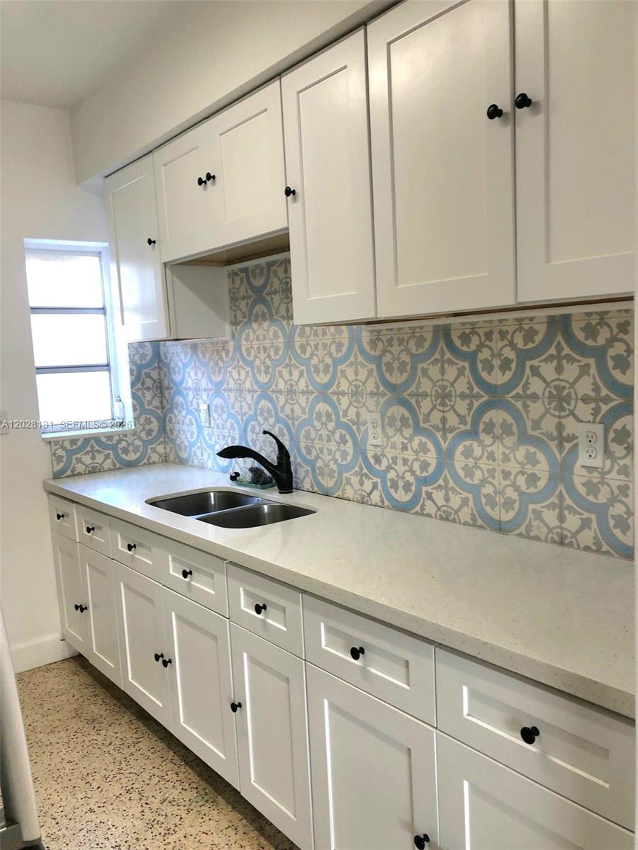 A kitchen features white cabinets, a light countertop, and a blue and white patterned backsplash — 7135 Rue Granville # 4, Miami Beach FL 33141, MIAMI BEACH, FL