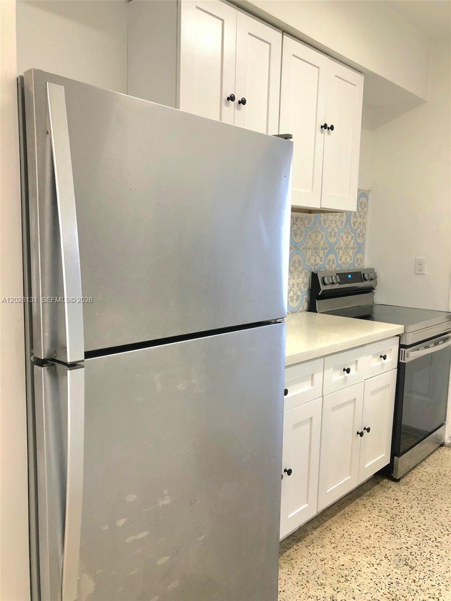 A stainless steel refrigerator stands next to white cabinets and a stove in a kitchen — 7135 Rue Granville # 4, Miami Beach FL 33141, MIAMI BEACH, FL