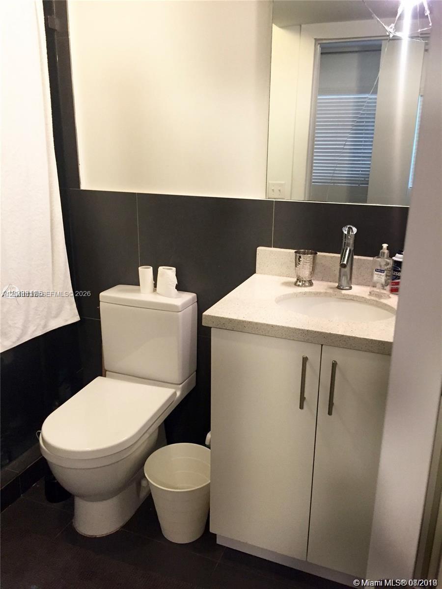 A bathroom features a white vanity with a stone countertop, a toilet, and dark wall tiles — 1600 Euclid Ave # 203, Miami Beach FL 33139, MIAMI BEACH, FL