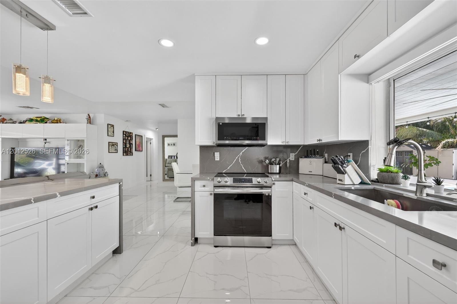 A modern white kitchen features gray marble-veined countertops, stainless steel appliances, and glossy tile flooring — 14234 SW 75th Ter, Miami FL 33183, MIAMI, FL