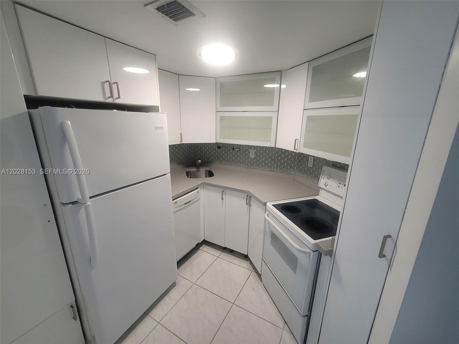 A small kitchen features white cabinets, white appliances, gray countertops, and light-colored tile flooring — 2600 Collins Ave # 411, Miami Beach FL 33140, MIAMI BEACH, FL