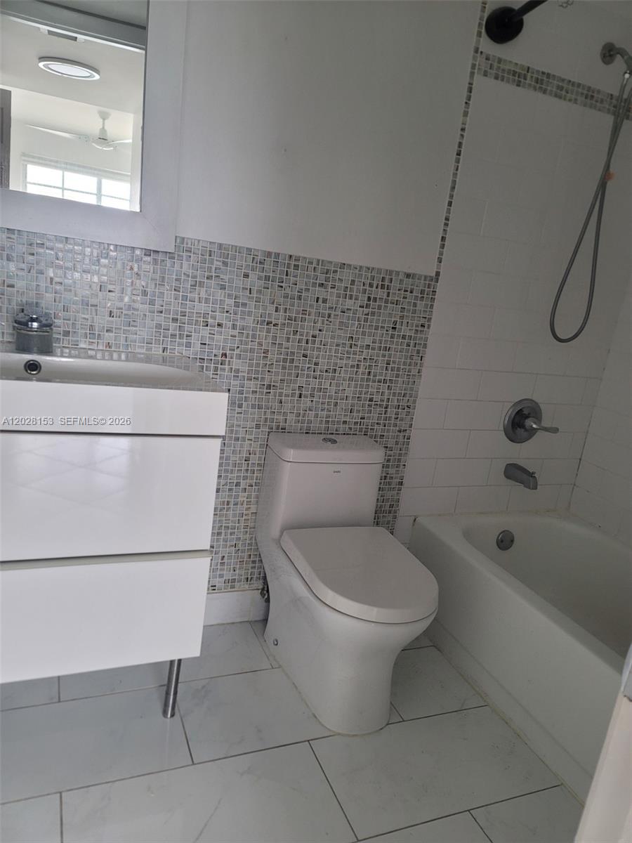A bathroom features a white vanity, a toilet, and a bathtub with tiled walls — 2600 Collins Ave # 411, Miami Beach FL 33140, MIAMI BEACH, FL