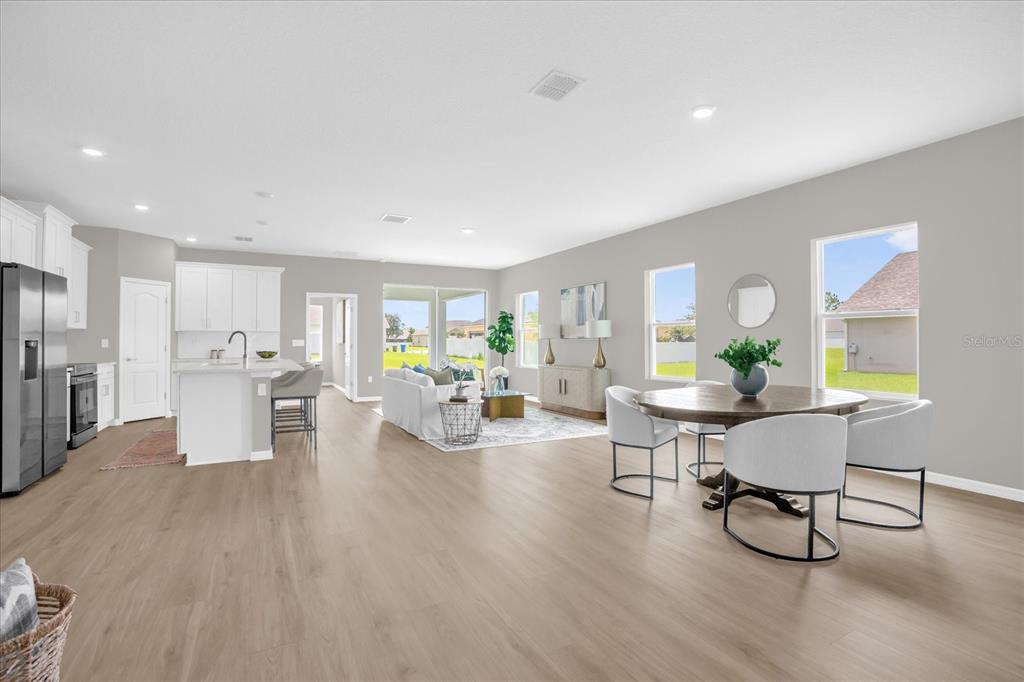 An open-concept living and dining area features light wood flooring, white cabinetry, and large windows — 6932 SAN BRUNO DRIVE, SEBRING, FL