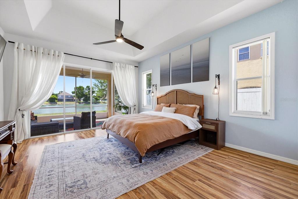 A bedroom with wood floors and curtains opens to a screened patio overlooking a lake — 6223 ROCK CREEK CIRCLE, ELLENTON, FL