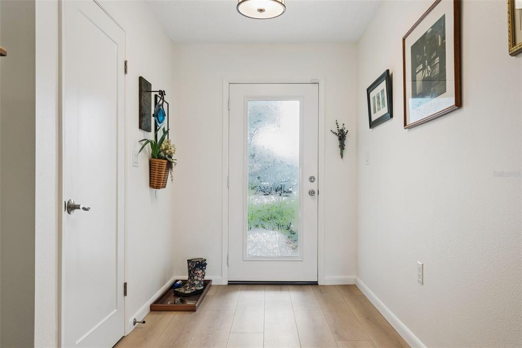 A bright entryway features light wood flooring, a white front door, and framed wall art — 4521 EDITH STREET, NEW PORT RICHEY, FL