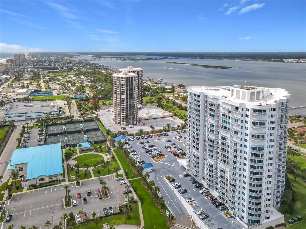 An aerial view shows two high-rise residential buildings, tennis courts, and a parking lot — 2 OCEANS WEST BLVD UNIT 300, DAYTONA BEACH SHORES, FL