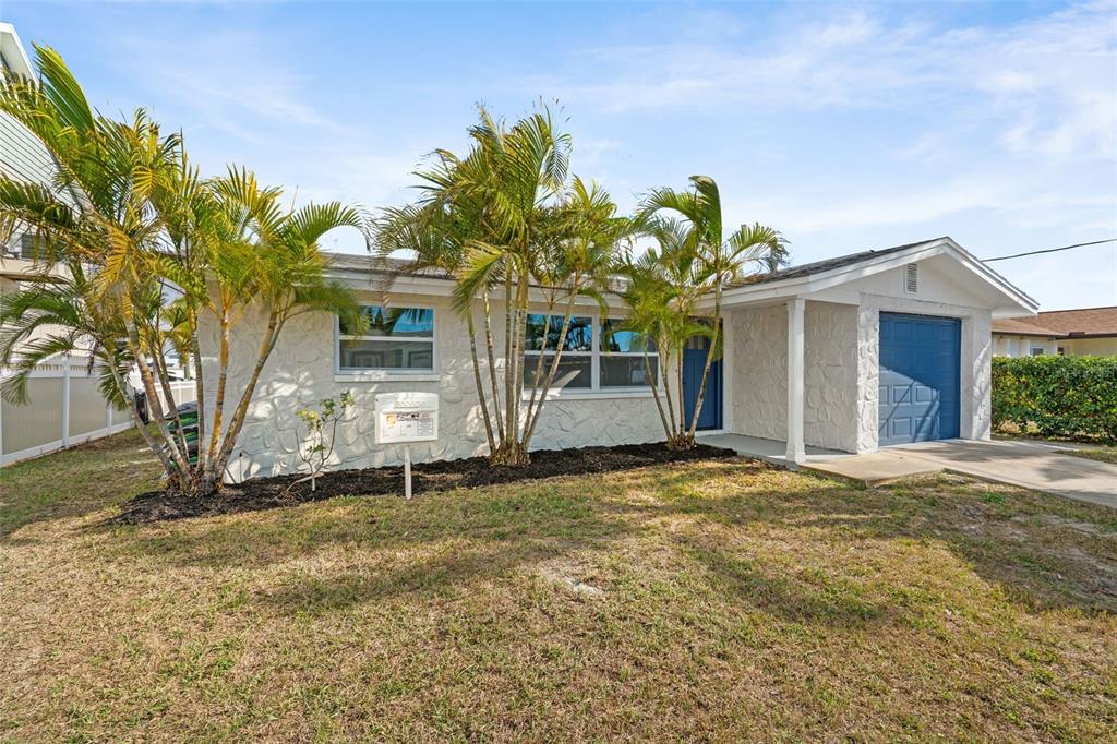 A single-story house with a white stone facade, blue garage door, and palm trees — 13804 VICTOR AVENUE, HUDSON, FL