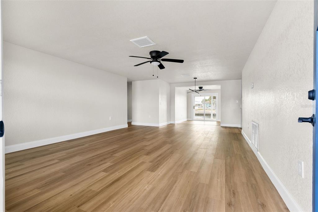 An open-concept living area features light wood-look flooring, white walls, and two ceiling fans — 13804 VICTOR AVENUE, HUDSON, FL