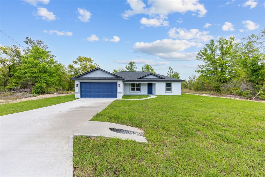 A single-story house with a blue garage door, white siding, and a concrete driveway — 5 MALAUKA LOOP TRACK, OCKLAWAHA, FL