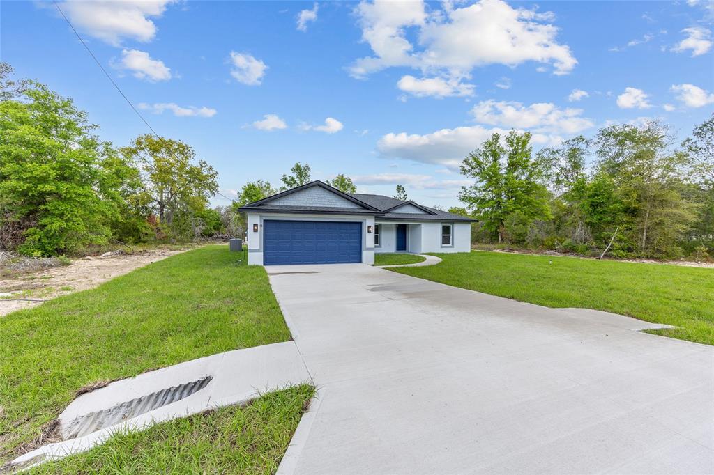 A single-story house with a blue garage door sits on a grassy lot — 5 MALAUKA LOOP TRACK, OCKLAWAHA, FL