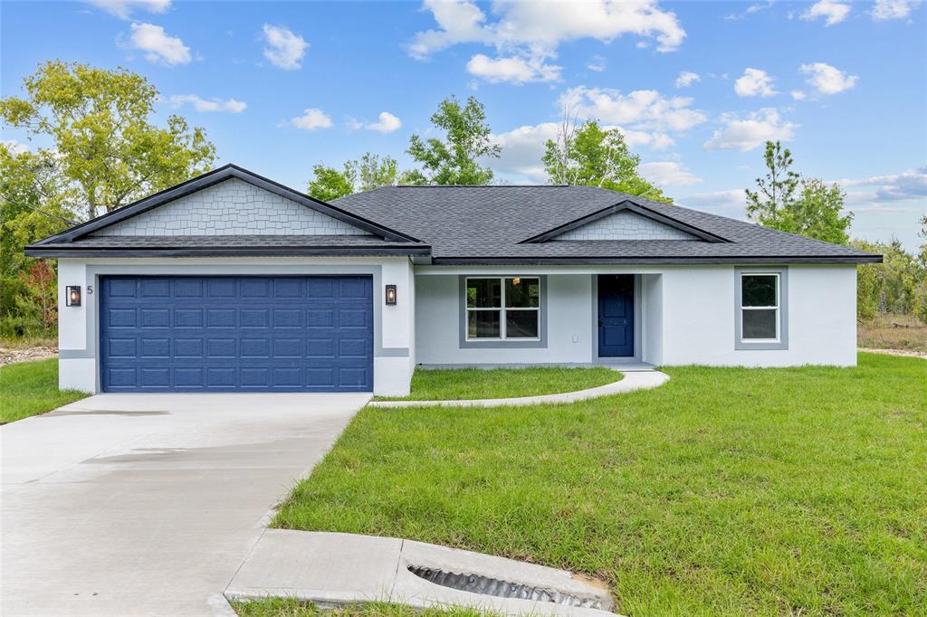 A single-story house with a blue garage door, white stucco walls, and a shingled roof — 5 MALAUKA LOOP TRACK, OCKLAWAHA, FL