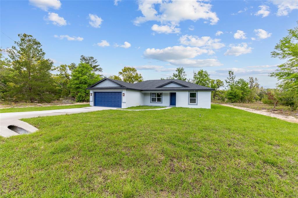 A single-story house with a blue garage door and white exterior sits on a lawn — 5 MALAUKA LOOP TRACK, OCKLAWAHA, FL