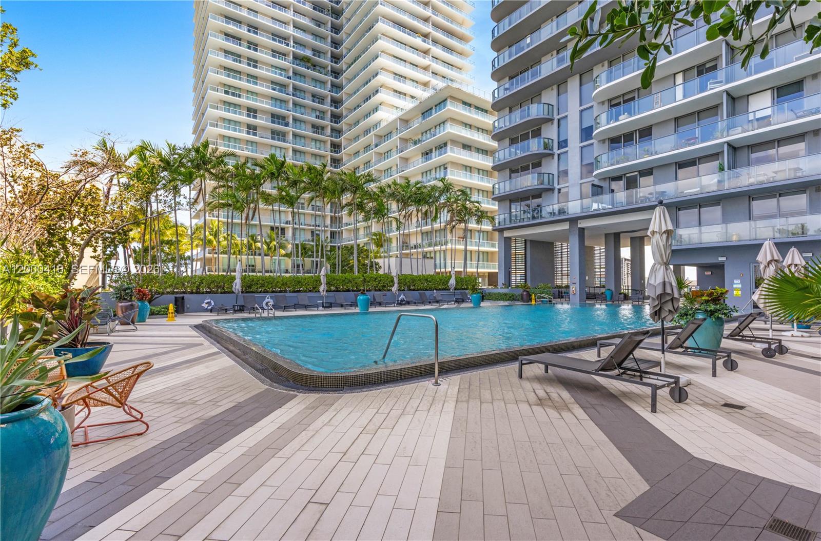 A swimming pool area with lounge chairs, palm trees, and modern high-rise buildings — 121 NE 34th St # 2602, Miami FL 33137, MIAMI, FL