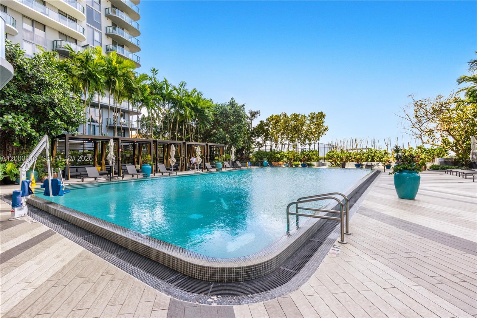 A large rectangular swimming pool features a tiled deck, lounge cabanas, and surrounding palm trees — 121 NE 34th St # 2602, Miami FL 33137, MIAMI, FL