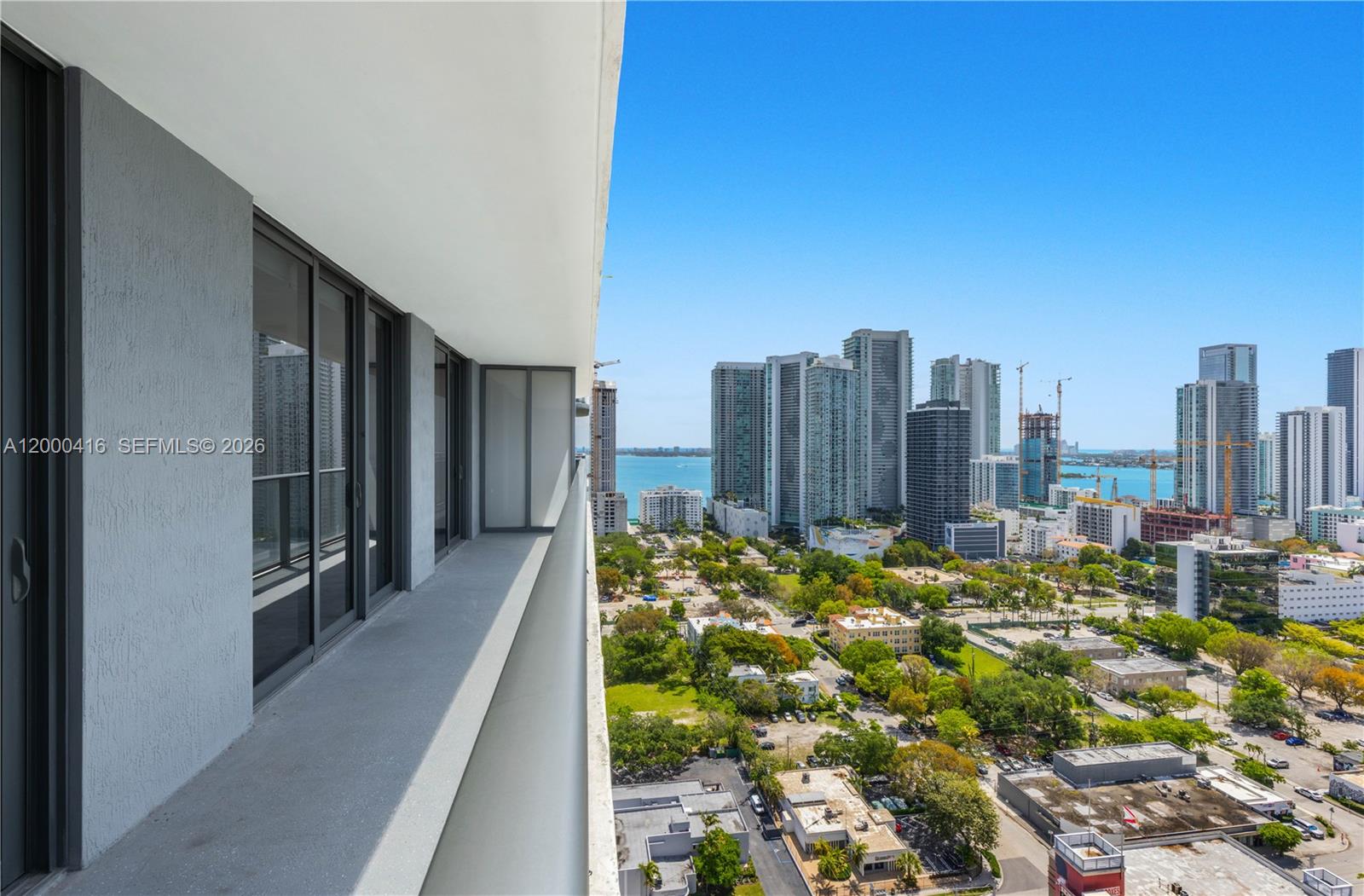 A high-rise balcony overlooks a city skyline, green spaces, and a body of water — 121 NE 34th St # 2602, Miami FL 33137, MIAMI, FL