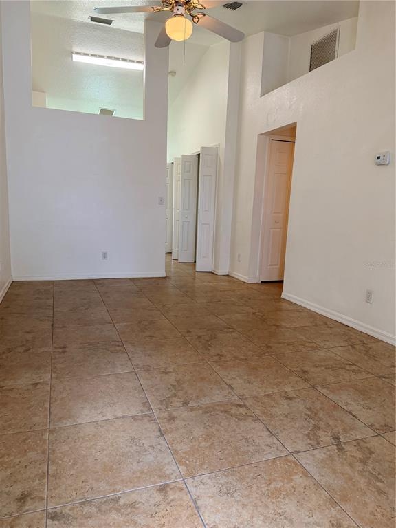 An empty room with tan tile flooring, white walls, a ceiling fan, and multiple doorways — 730 S GRAND HIGHWAY, CLERMONT, FL