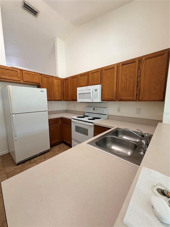 A kitchen features wood cabinets, white appliances, a double sink, and beige countertops — 730 S GRAND HIGHWAY, CLERMONT, FL