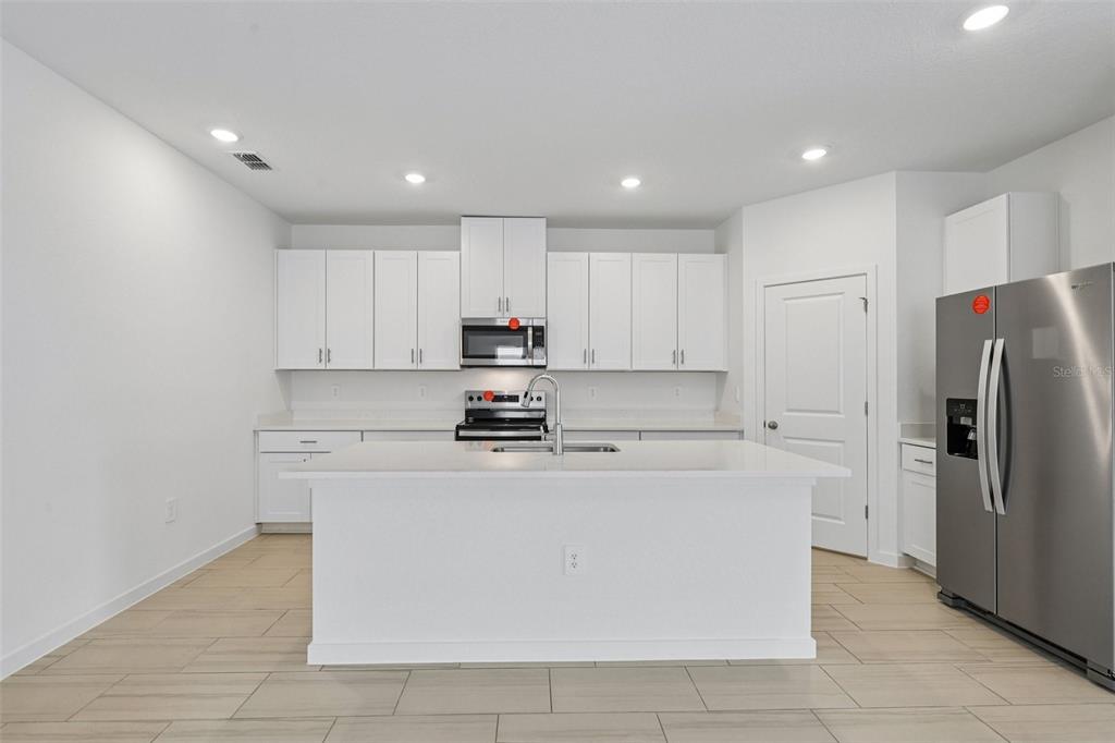 A modern kitchen features white cabinets, stainless steel appliances, a central island, and tile flooring — 71 ARARAT DRIVE, PALM COAST, FL
