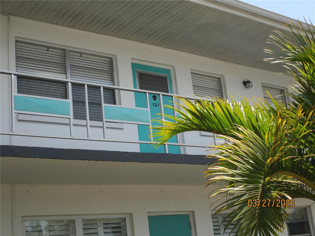 An exterior view of a second-story apartment balcony with a teal door and railing — 6055 21ST STREET N UNIT 12, ST PETERSBURG, FL