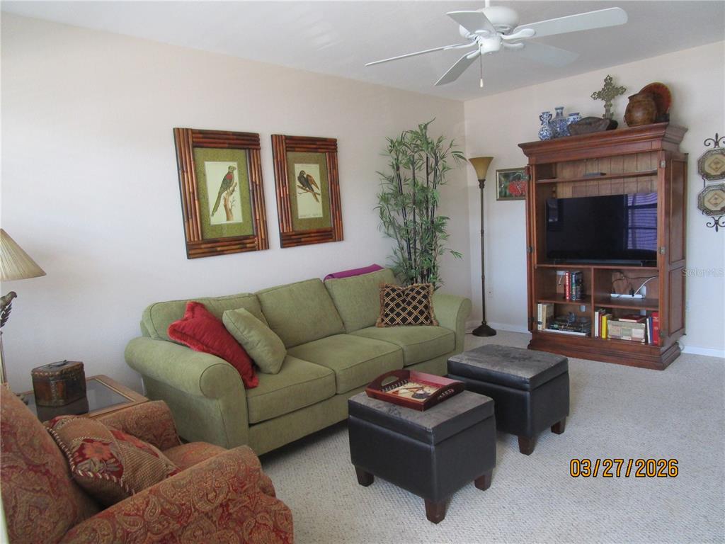 A living room features a green sofa, two dark ottomans, and a wooden entertainment center — 6055 21ST STREET N UNIT 12, ST PETERSBURG, FL