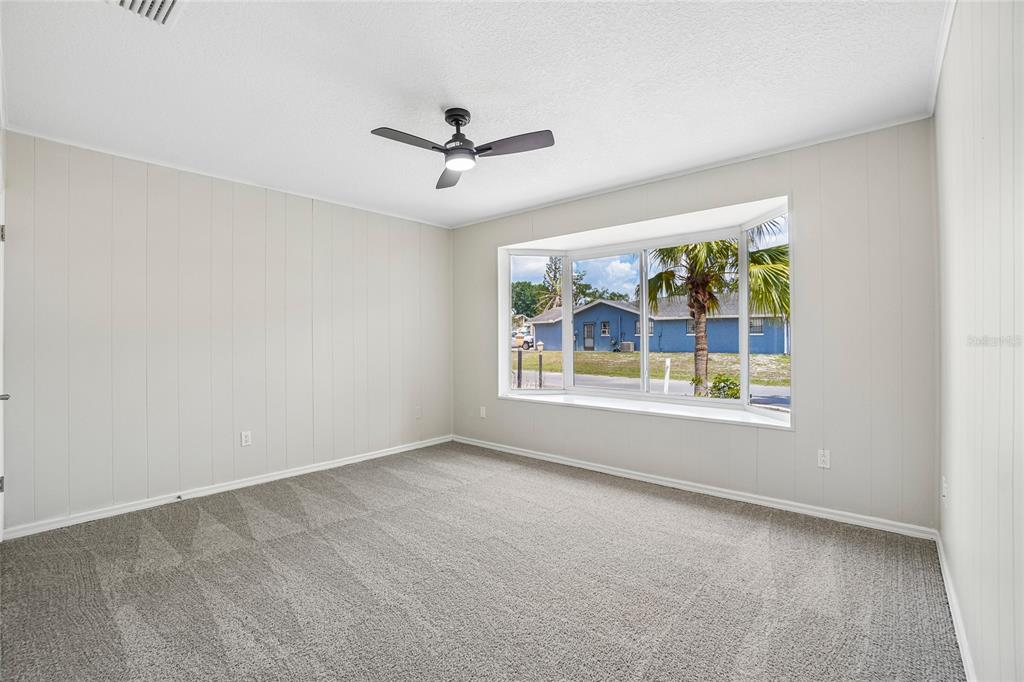 An empty bedroom features light-colored paneled walls, gray carpeting, a ceiling fan, and a bay window — 5609 EXECUTIVE DRIVE, NEW PORT RICHEY, FL