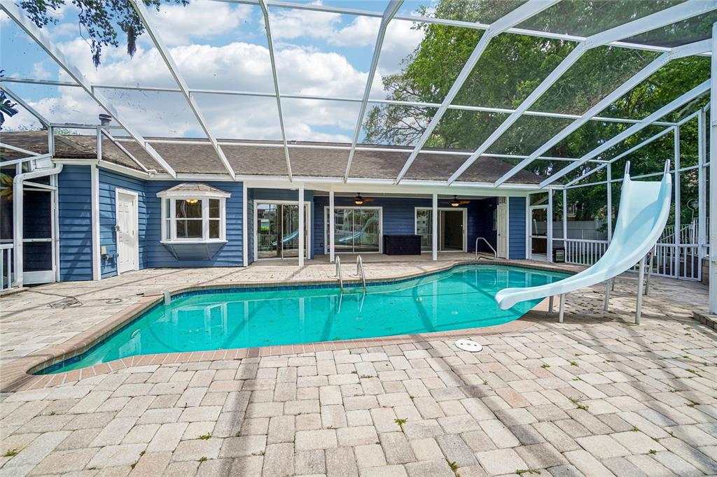 A blue house with a screened-in pool and a slide on a paved patio — 5609 EXECUTIVE DRIVE, NEW PORT RICHEY, FL