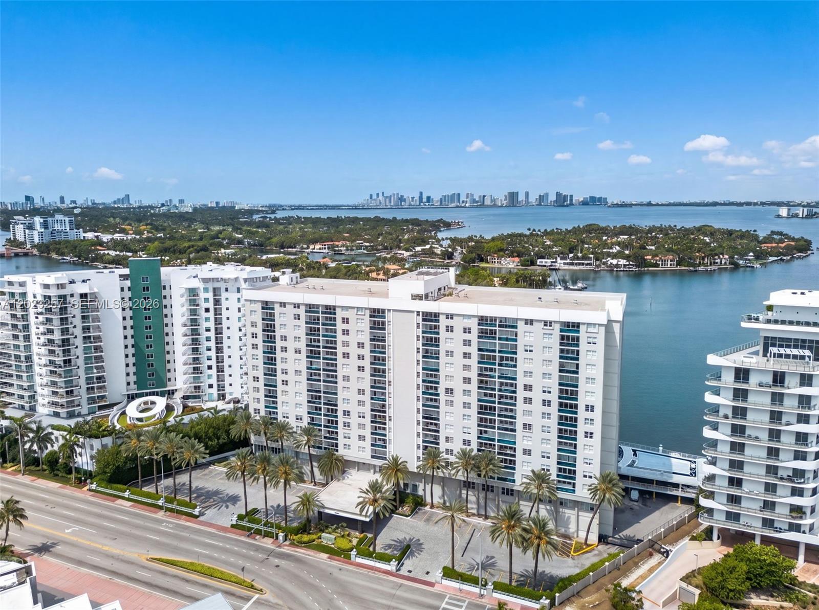 An aerial view shows a large white apartment building with palm trees near a bay — 6770 Indian Creek Dr # 5D, Miami Beach FL 33141, MIAMI BEACH, FL